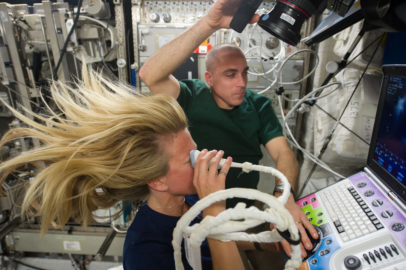 Astronaut Karen Nyberg holds an ultrasound probe to her eye while Chris Cassidy operates the ultrasound console in the Destiny laboratory of the International Space Station