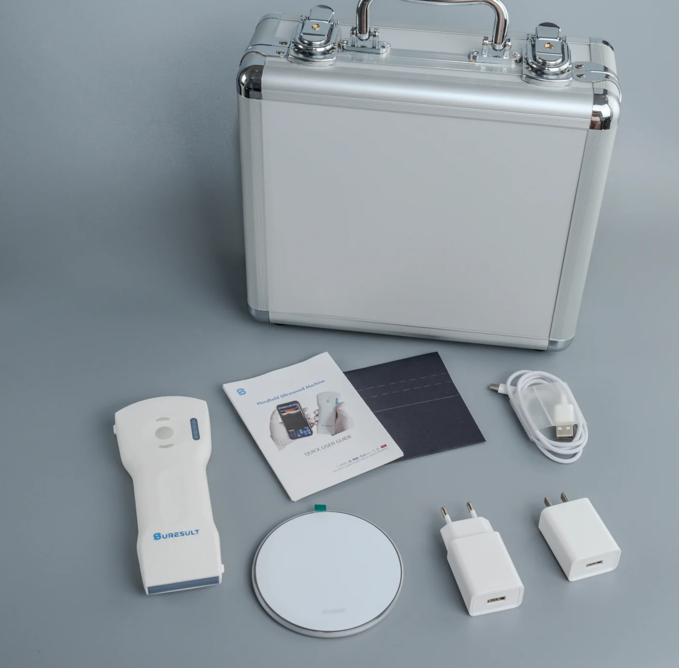 Een Suresult handheld echoprobe met bijbehorende aluminium koffer, beknopte handleiding, draadloze oplaadpad, EU- en VS-stekkers en oplaadkabel